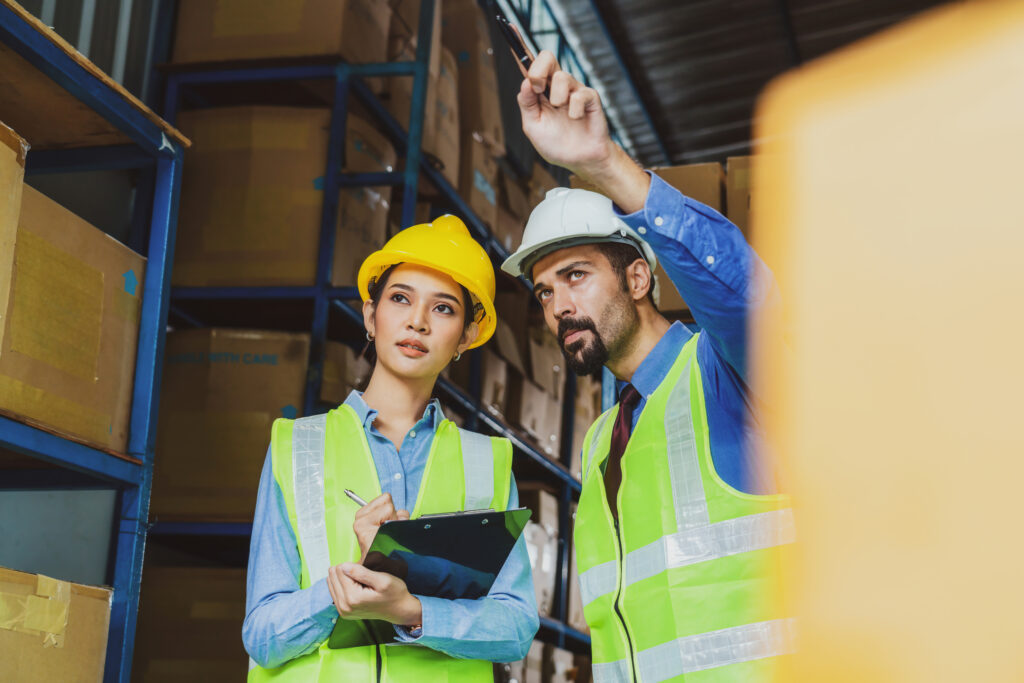 Le directeur de l'ouvrier d'entrepôt affecte et commande en regardant sérieusement la femme directrice adjointe dans l'entrepôt ou l'usine locale, les caucasiens asiatiques et blancs, le concept de partenaire et de collègue travaillant ensemble